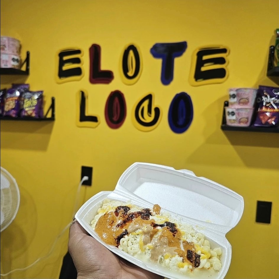 Marucha elote servida en charola frente a la pared amarilla de Elote Loco