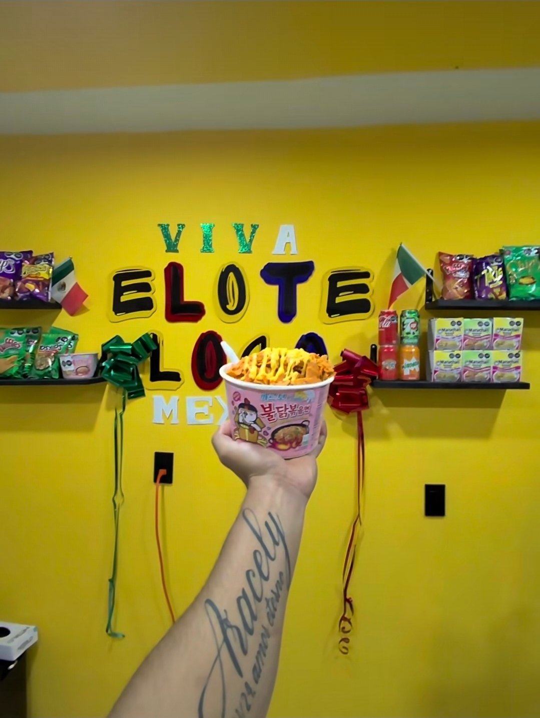 Buldak Lote preparado con queso amarillo frente a la pared de Elote Loco