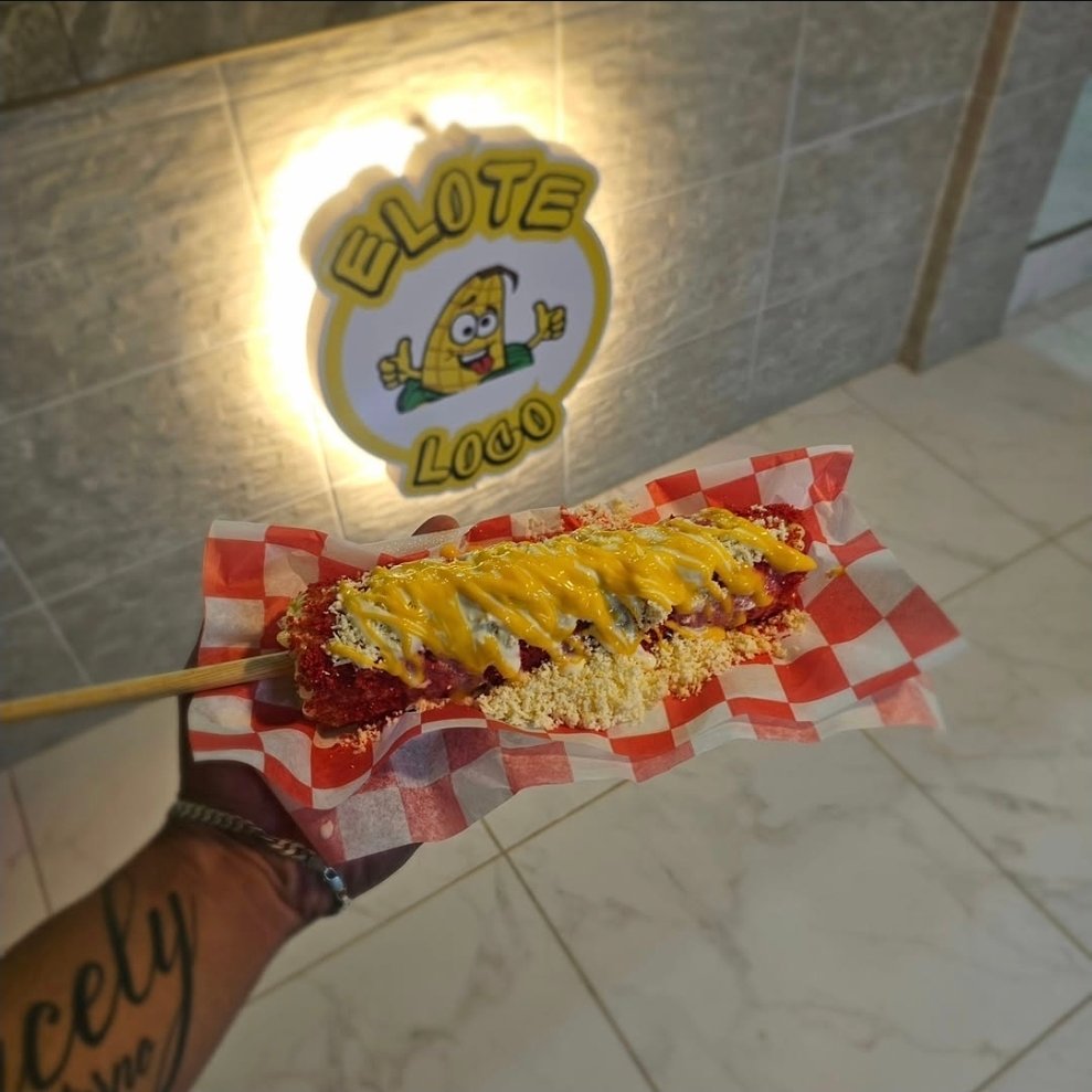 Elote entero loco con queso amarillo frente al letrero iluminado